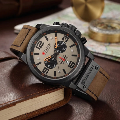 Black chronograph watch with grey dial and brown leather strap draped over a leather journal