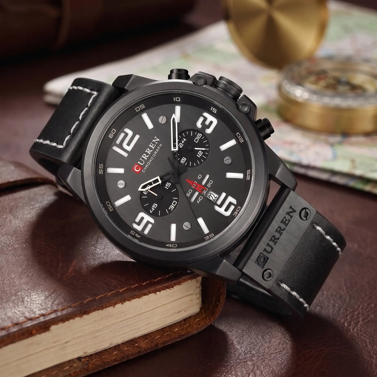Black chronograph watch with black dial and black leather strap draped over a leather journal