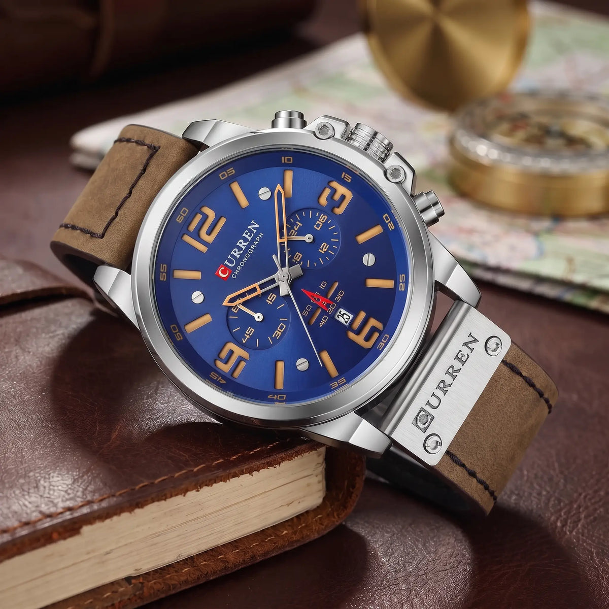 Silver chronograph watch with blue dial and brown leather strap draped over a leather journal