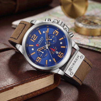 Silver chronograph watch with blue dial and brown leather strap draped over a leather journal
