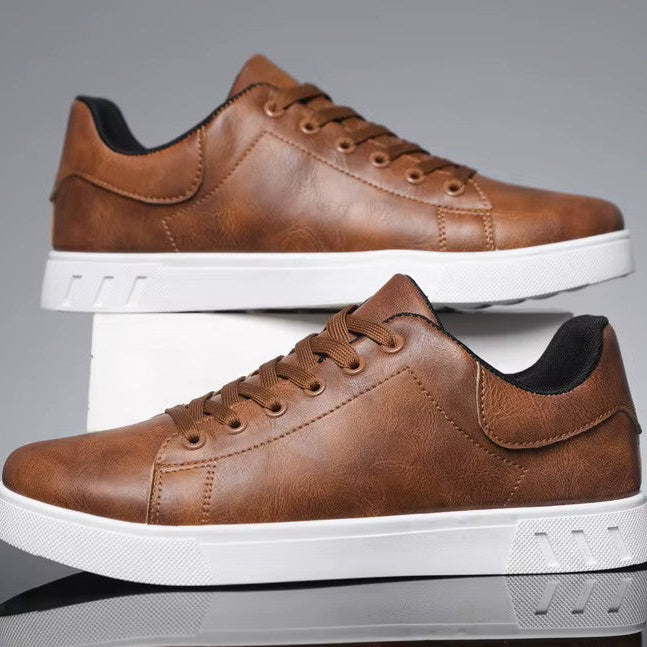 Pair of brown leather sneakers with white soles on a reflective surface.