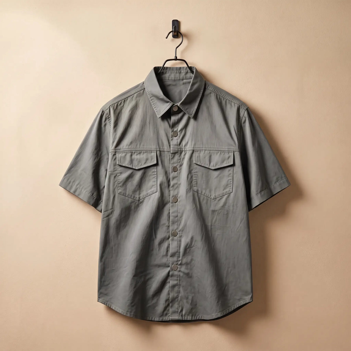 Gray short sleeve utility shirt on a black hanger against a sand plaster wall