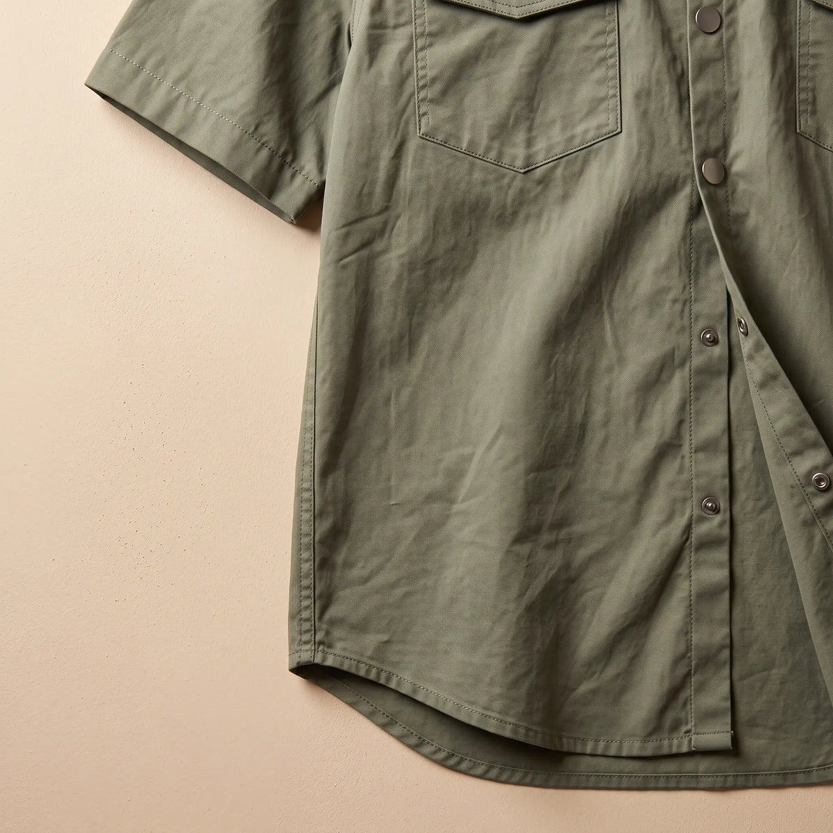 Close up of the short sleeve, side and curved hem on the green utility shirt laid flat