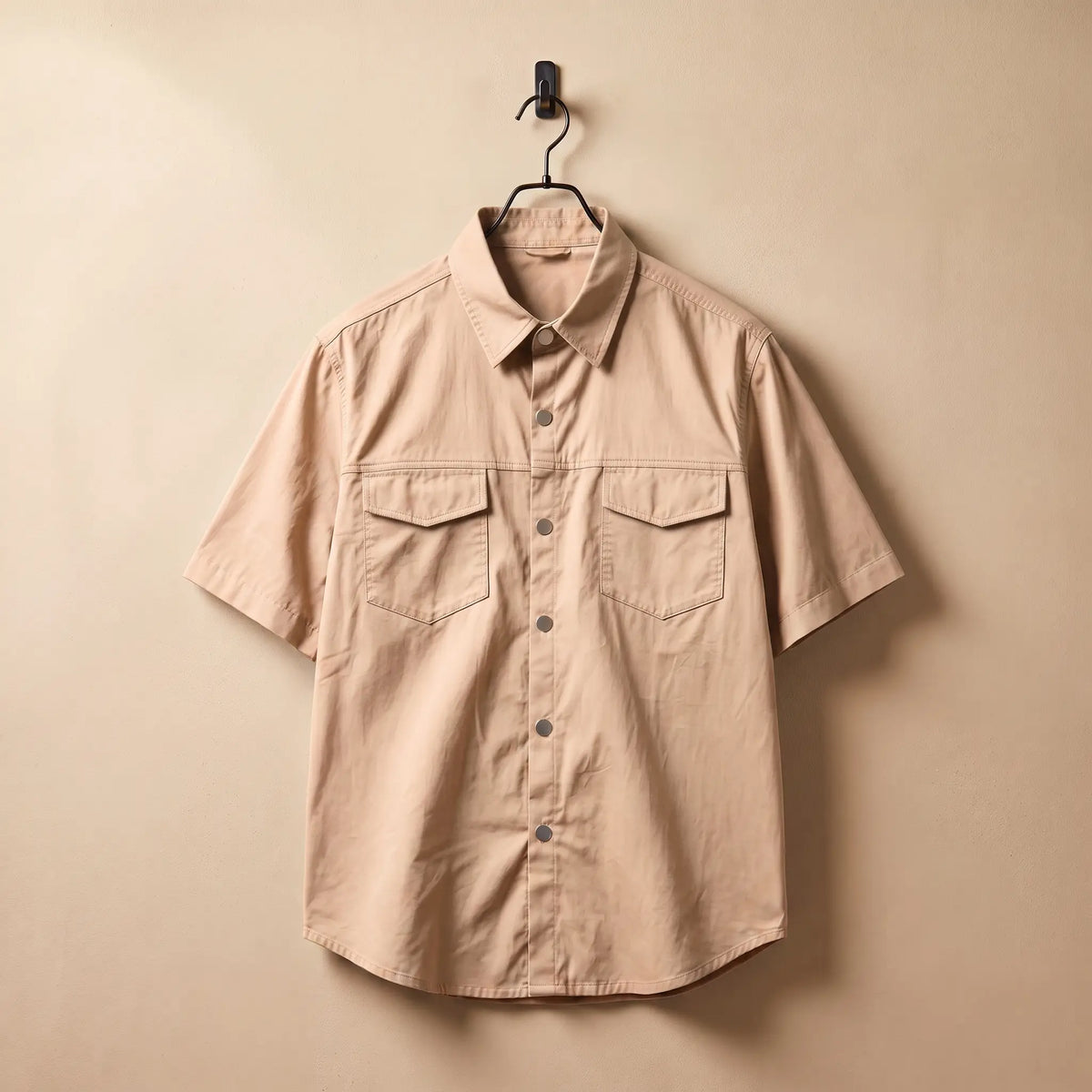 Khaki short sleeve utility shirt on a black hanger against a sand plaster wall