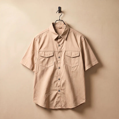 Khaki short sleeve utility shirt on a black hanger against a sand plaster wall