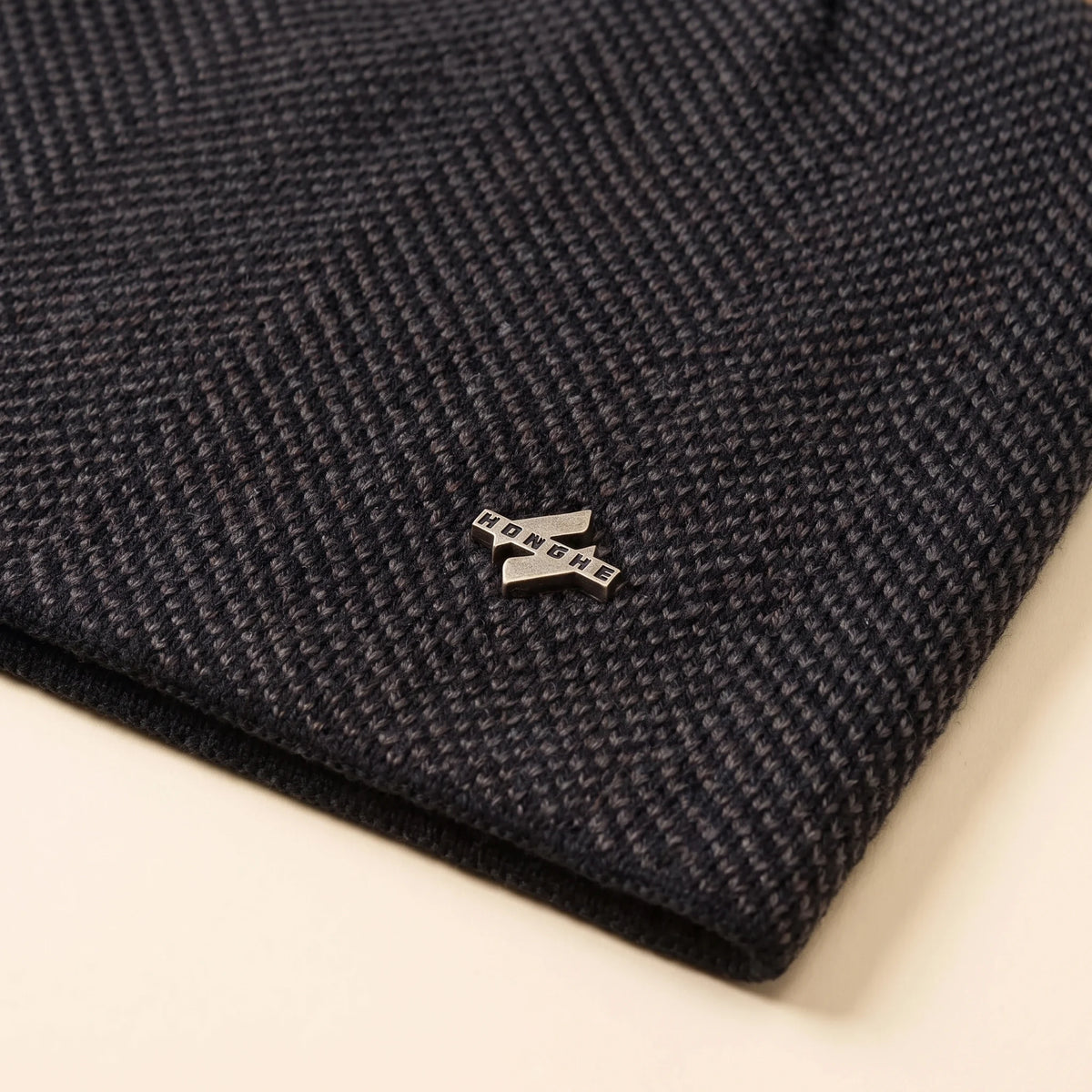 Close up of the herringbone knit, metal badge and black edge binding on the slouch knit beanie