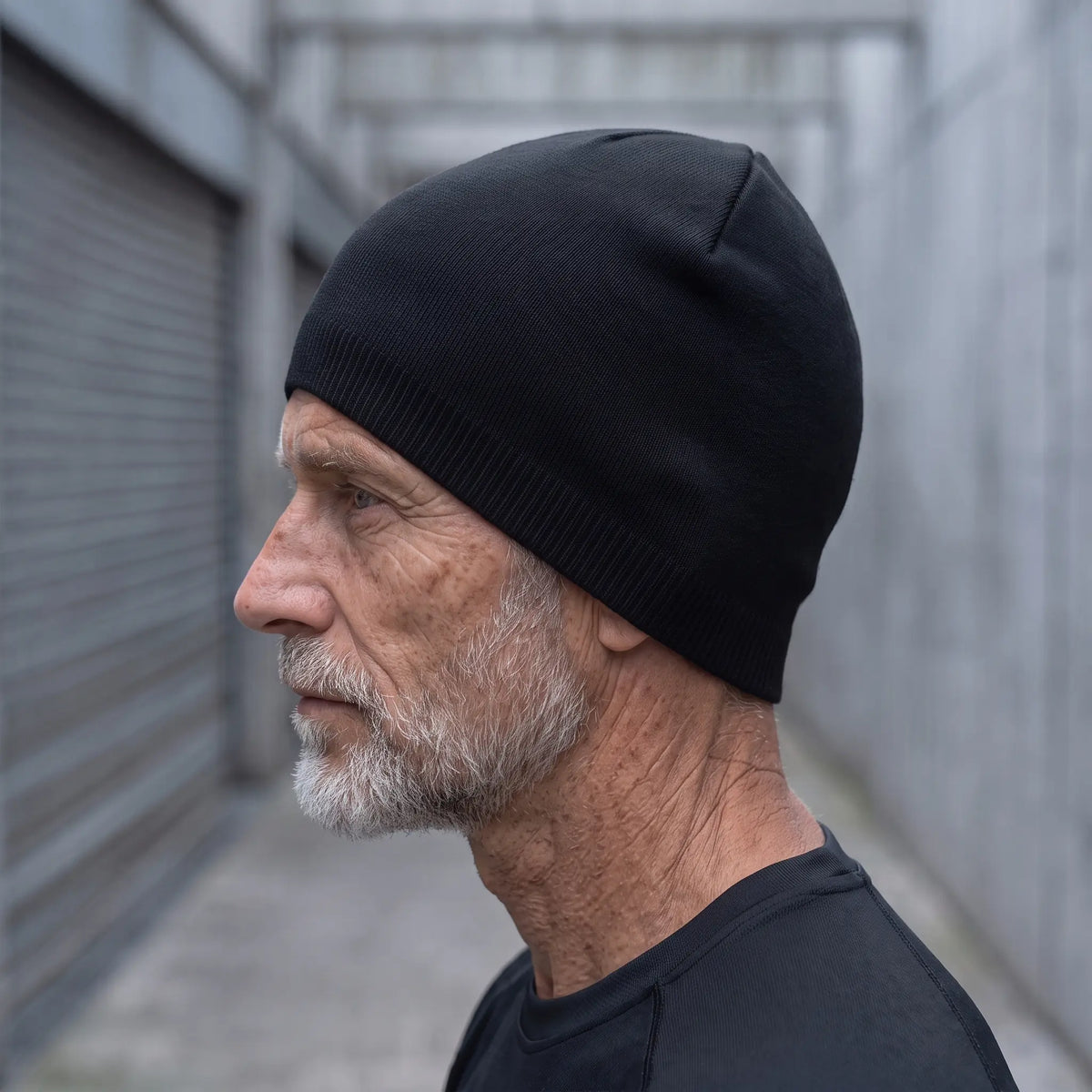 Smooth knit beanie in black worn side profile by an older man