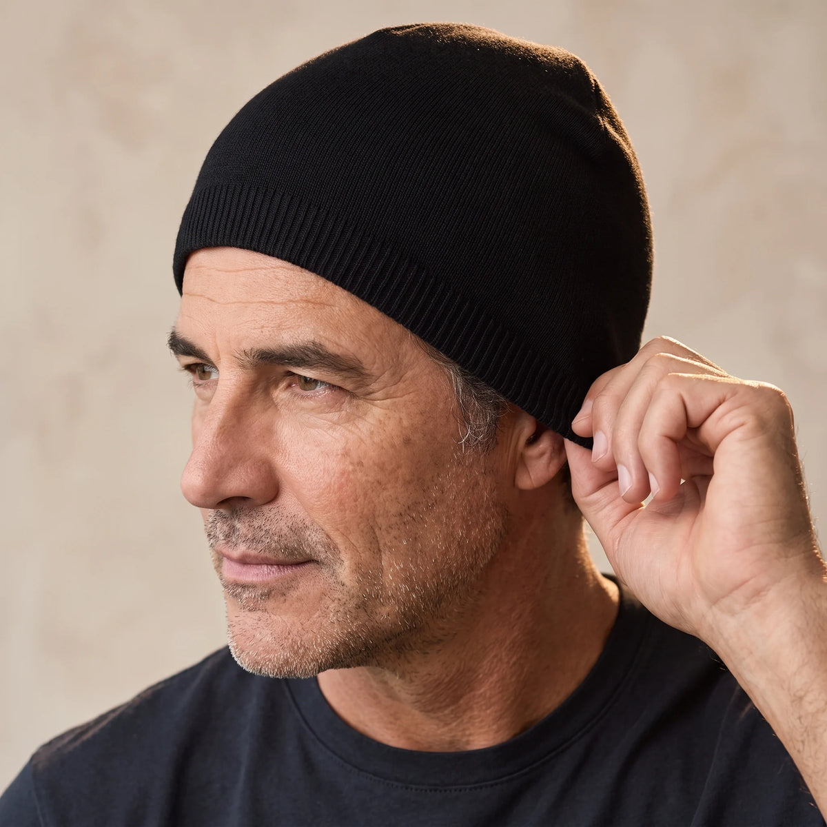 Man pulling the black smooth knit beanie down over his ear, men's fine knit winter beanie worn