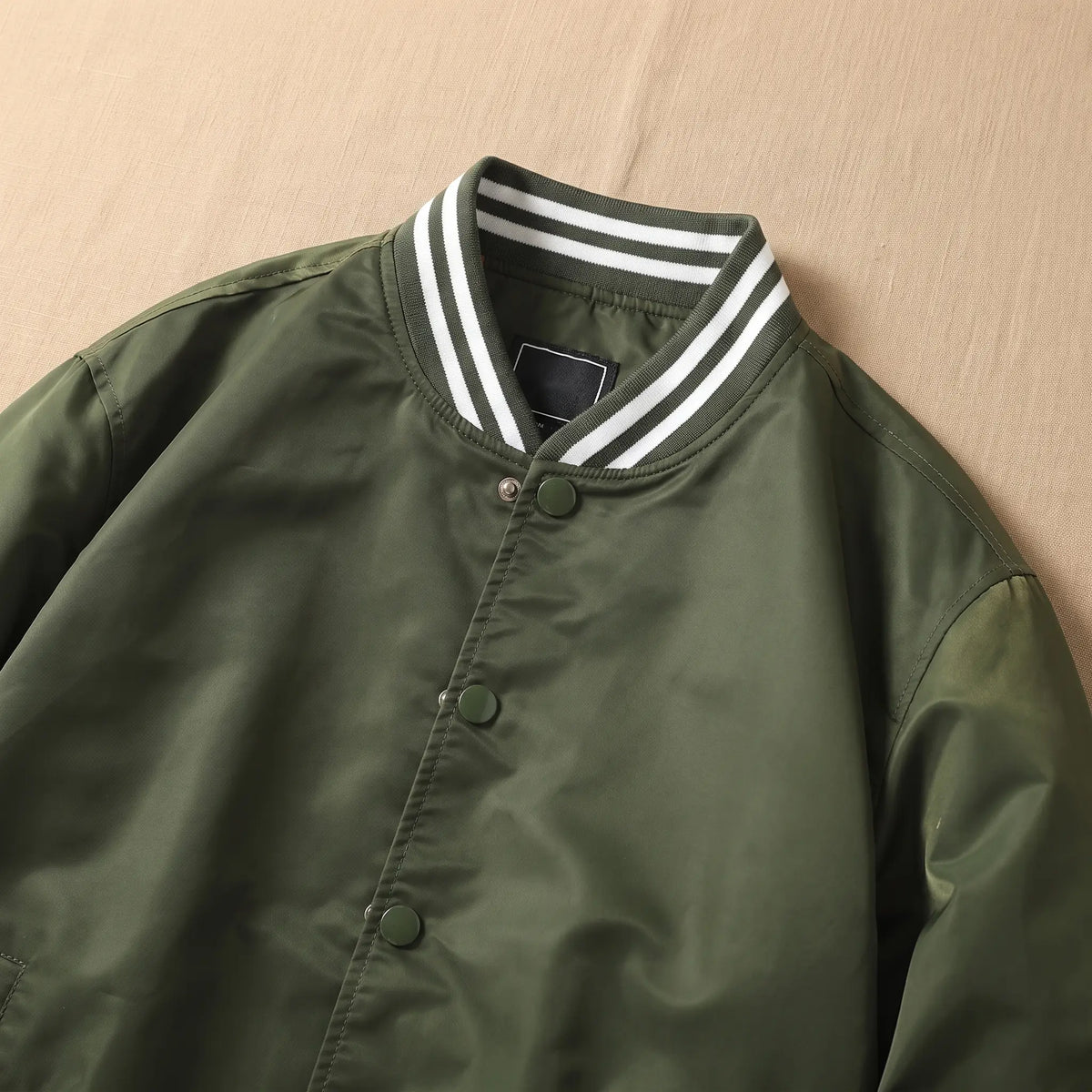 Close-up of green bomber jacket striped rib collar and metal snap front