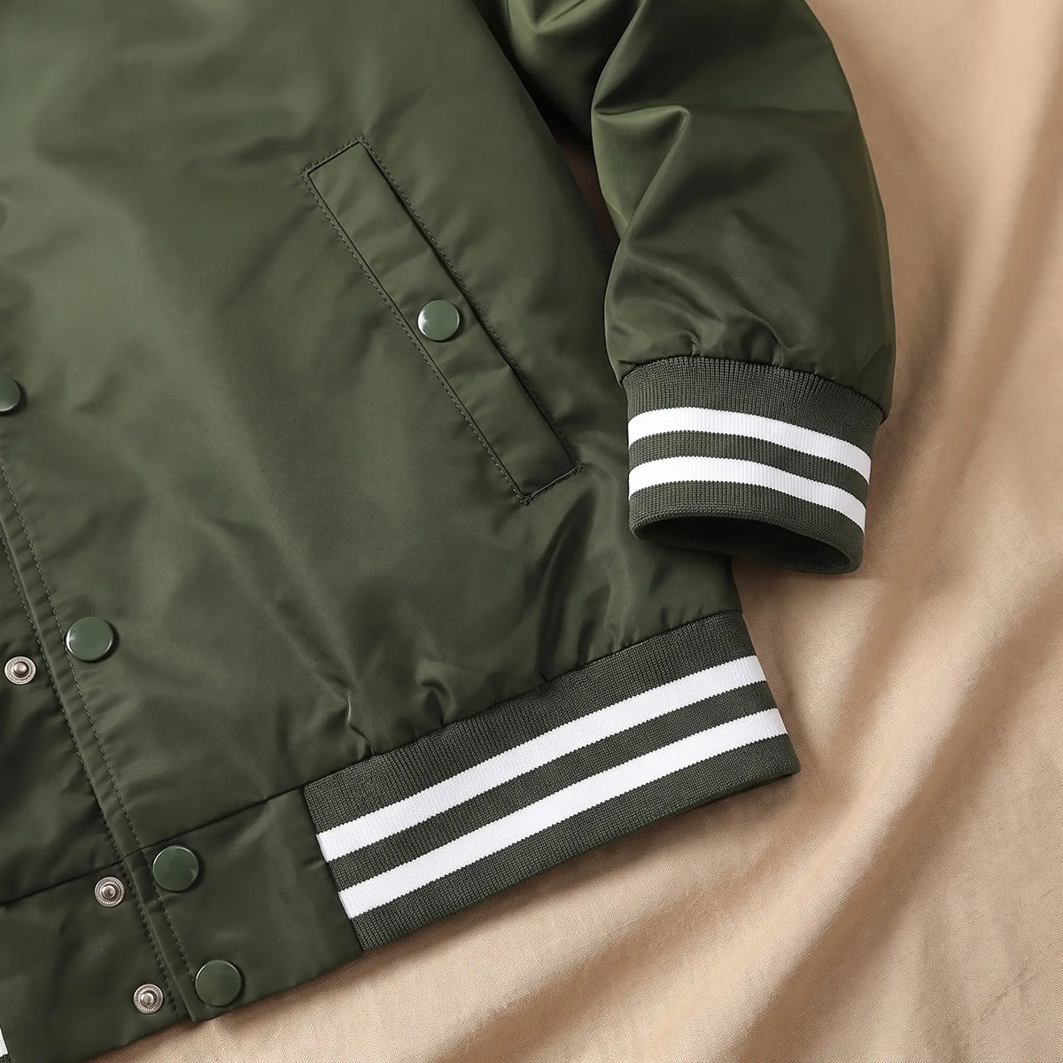 Close-up of green bomber jacket snap pocket, striped rib cuff and hem