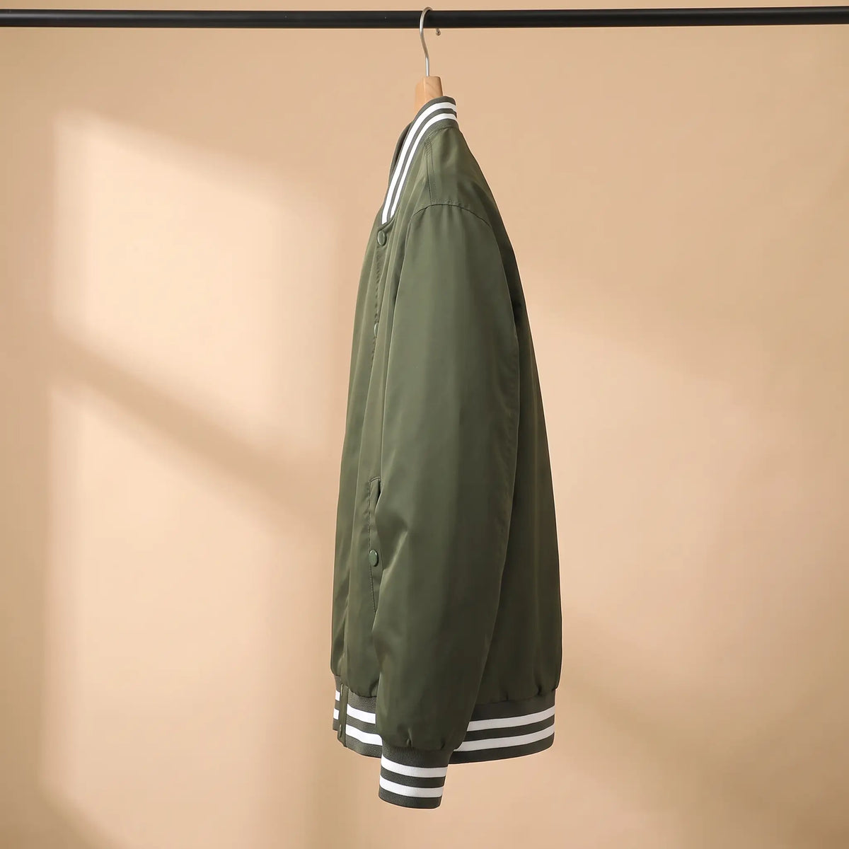 Side view of green snap-front bomber jacket on a wooden hanger