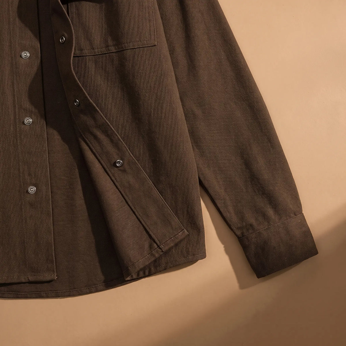 Snap Front Shirt in Brown laid flat, cuff and snap front hem close-up