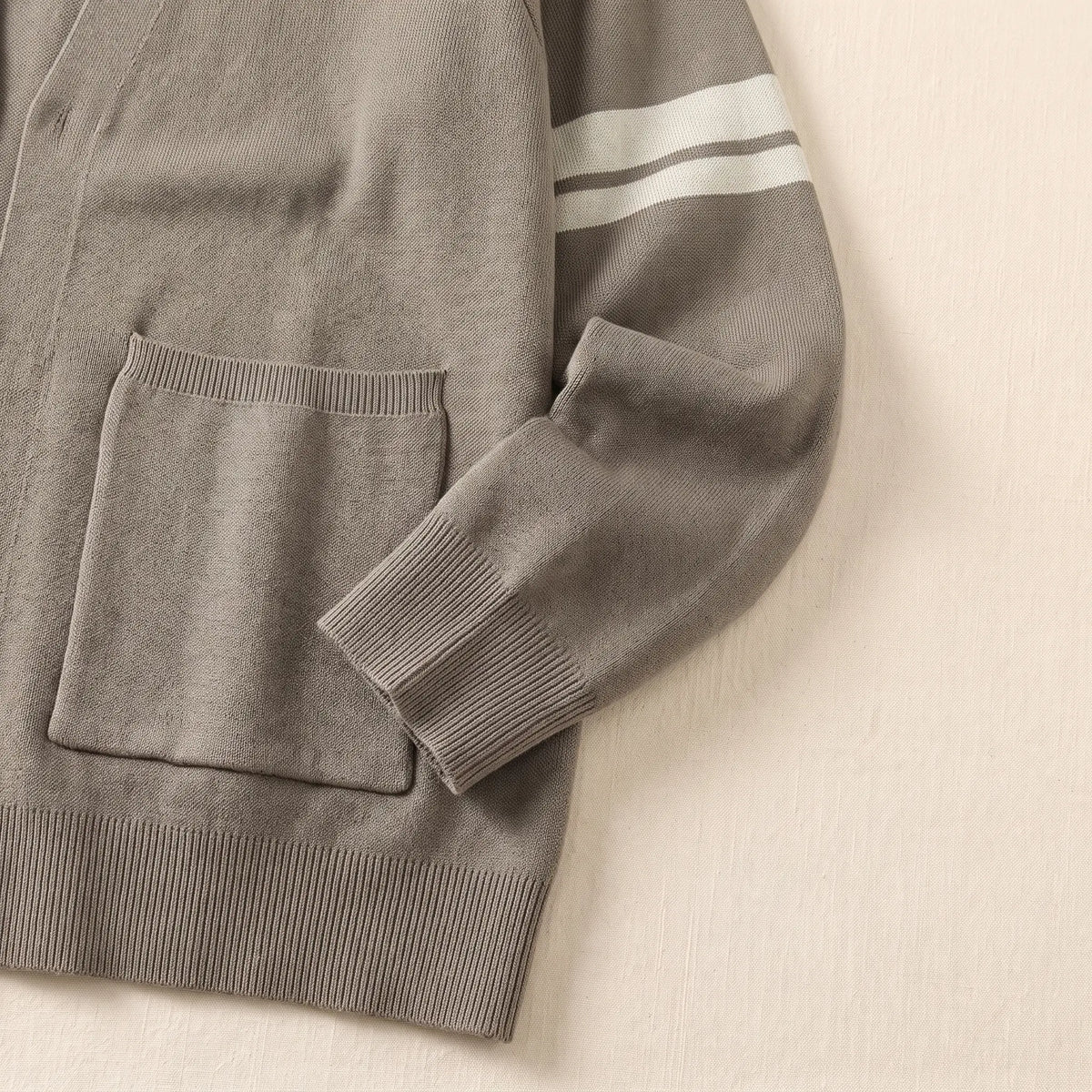 Close-up of men's khaki knit cardigan patch pocket, ribbed cuff and sleeve stripes