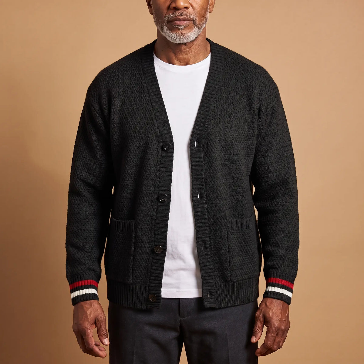 Man wearing the Stripe Cuff Cardigan in black, a textured knit V-neck cardigan with red and white striped cuffs, worn open over a white tee