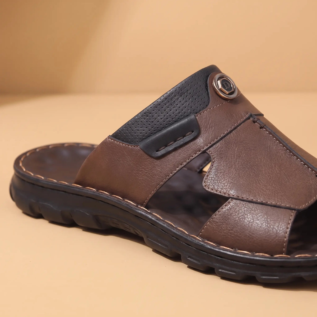 Close up of the metal emblem tab and contrast stitched panel seam on a brown mens slide