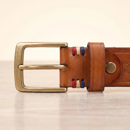 Close up of the antique brass pin buckle, keeper loop and red cream and blue cord wraps on the tan tooled cowhide belt