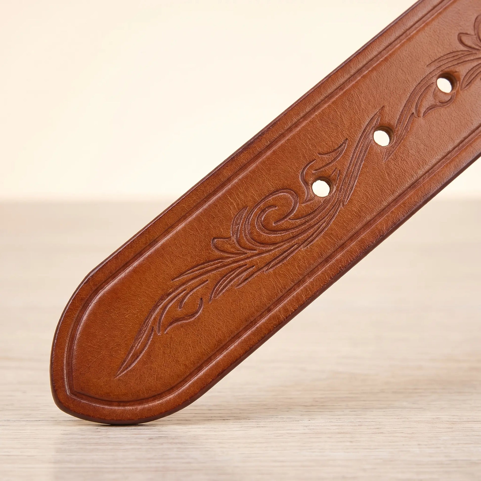 Close up of the embossed scroll tooling, burnished edge and punched holes on the tan tooled cowhide belt