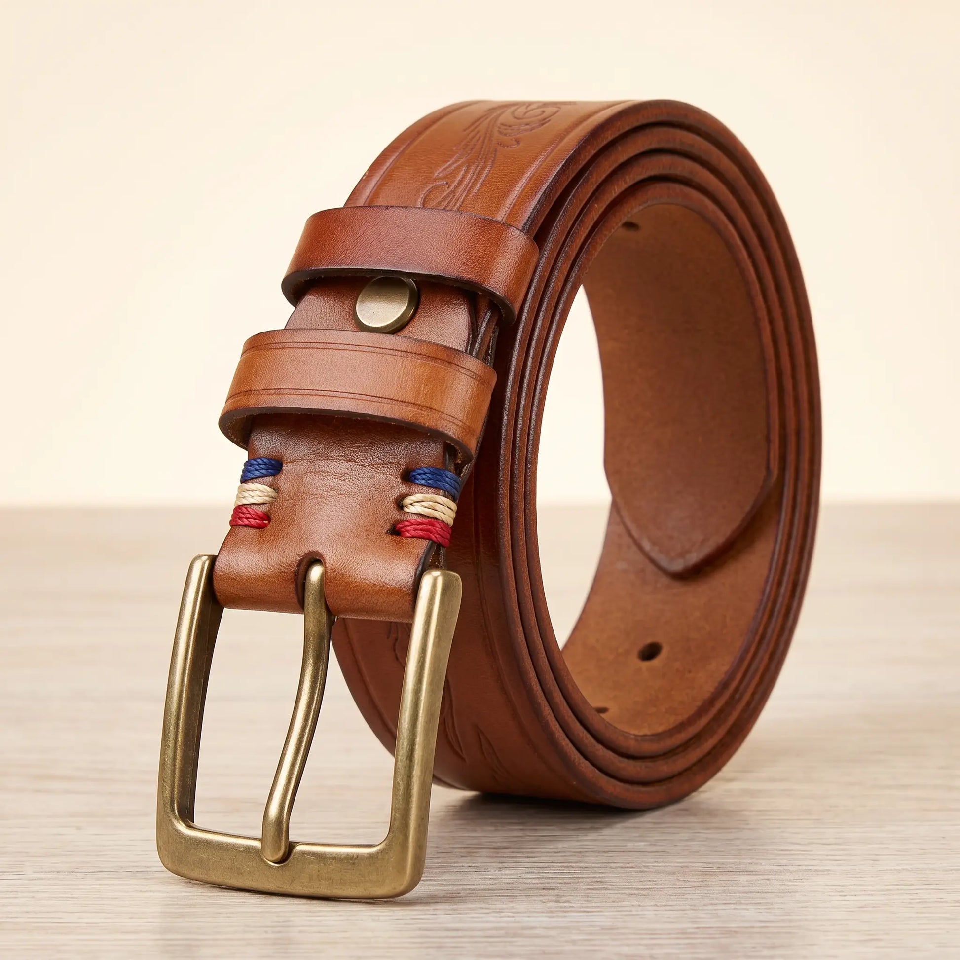 Tooled cowhide belt in tan with antique brass pin buckle and embossed scroll pattern