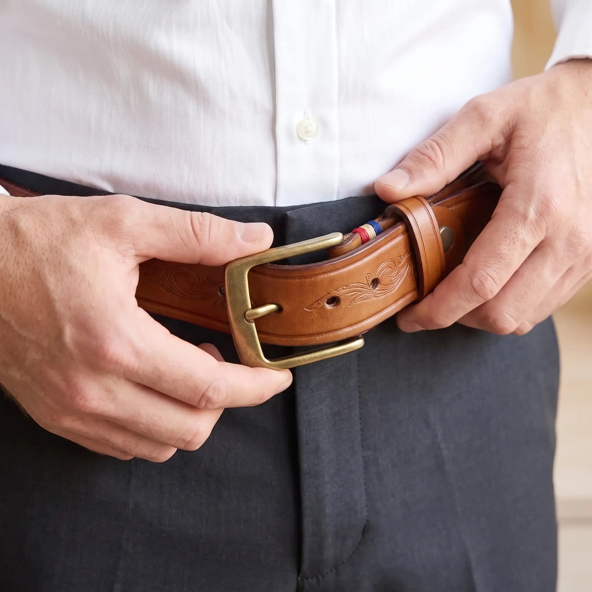 Man fastening the tan tooled cowhide belt at the waist over dark trousers and a white shirt