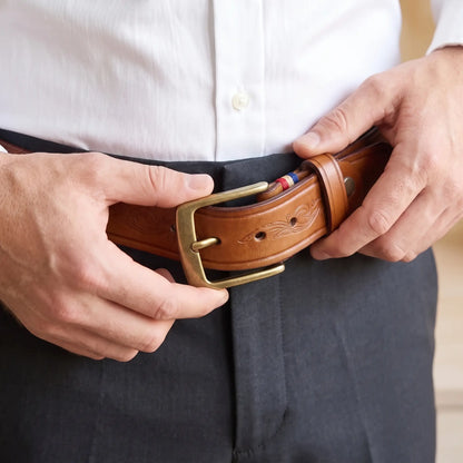 Man fastening the tan tooled cowhide belt at the waist over dark trousers and a white shirt