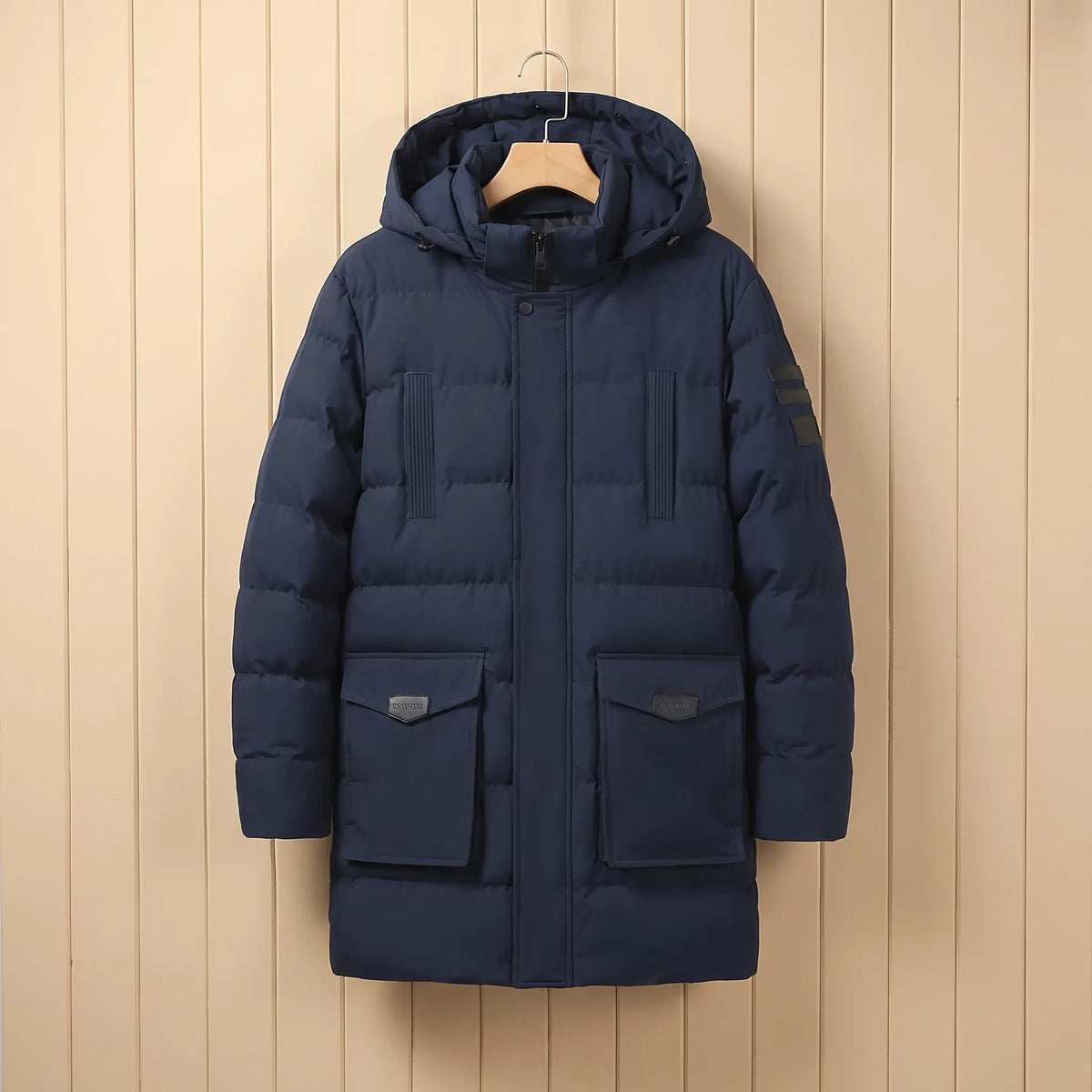 Men's navy blue quilted padded winter coat with hood, snap placket and large flap pockets on a wooden hanger