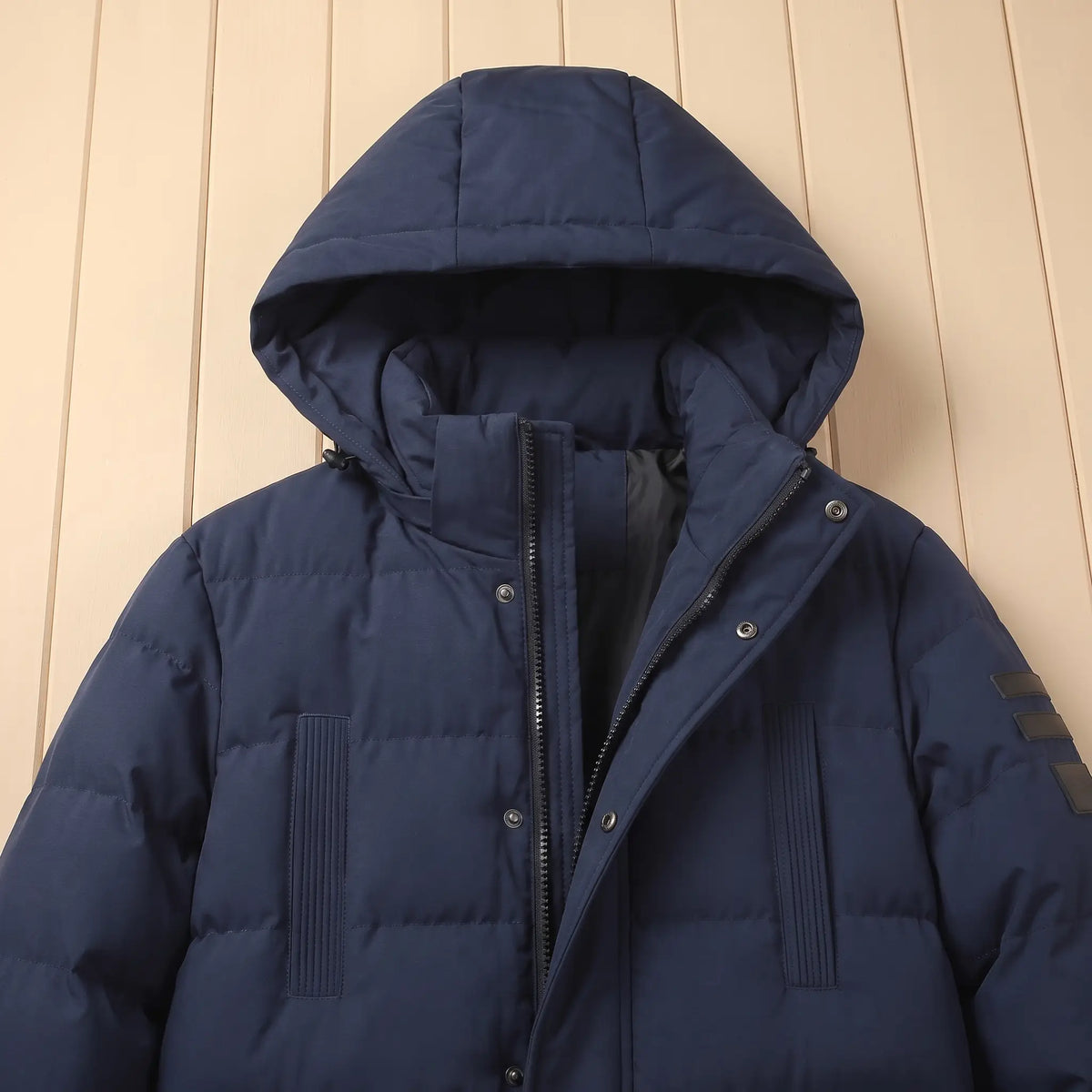 Close-up of navy quilted coat hood, stand collar, zip and snap placket