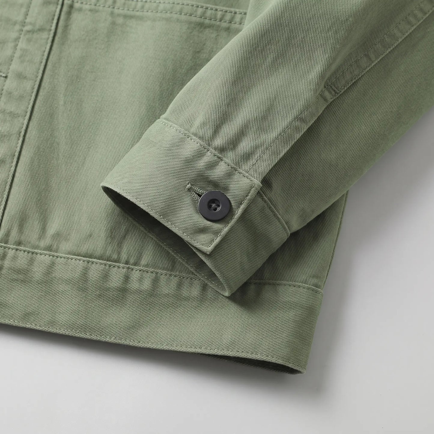 Close up of the buttoned cuff and straight hem on the green washed chore jacket