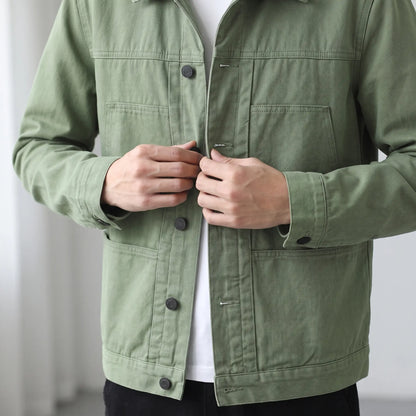 Man fastening a front button on the green washed chore jacket worn over a white tee