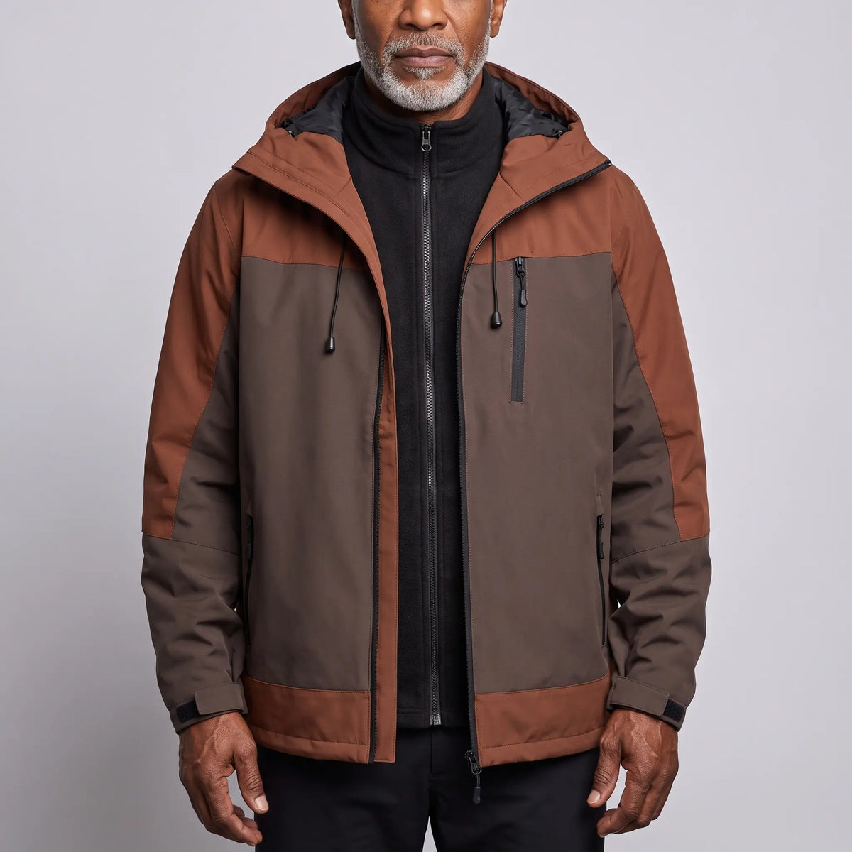 Men's brown waterproof hooded hiking jacket with rust shoulder panels, worn open over a black fleece
