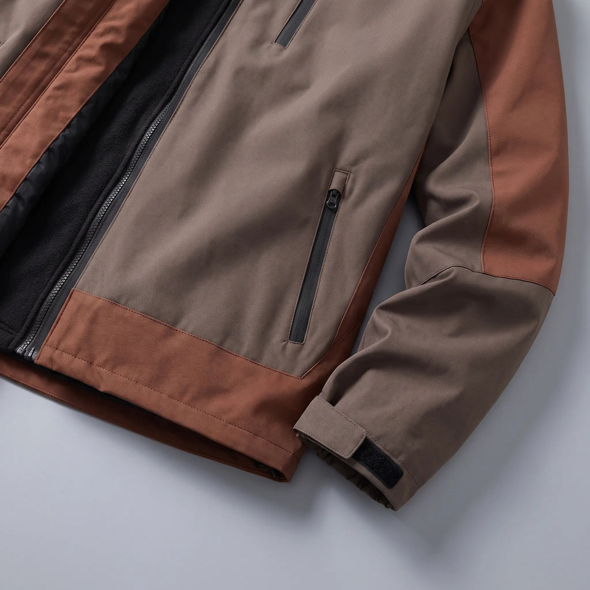 Close up of the zip hand pocket and adjustable cuff tab on the brown windproof hiking jacket