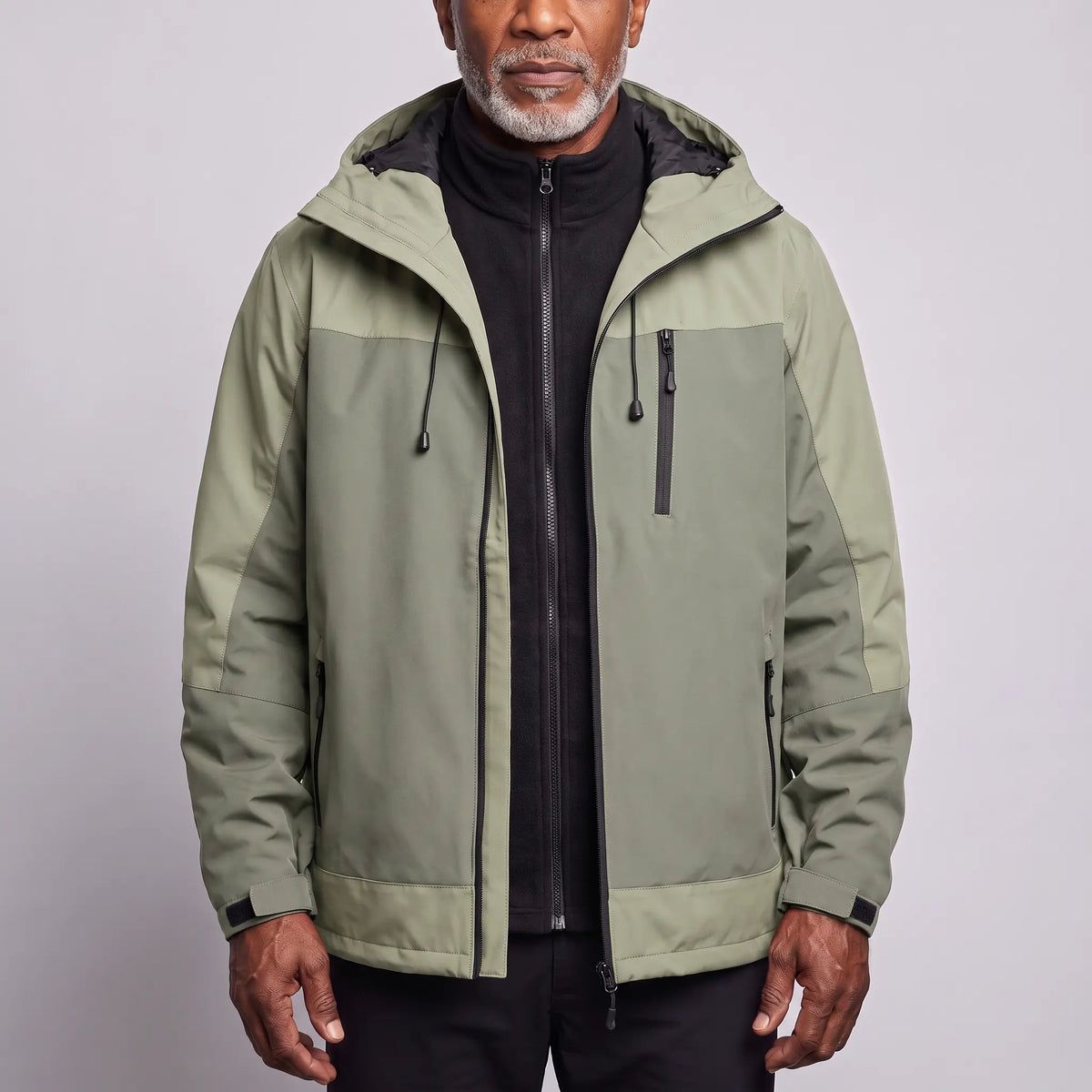 Men's green waterproof hooded hiking jacket in two tones of sage, worn open over a black fleece