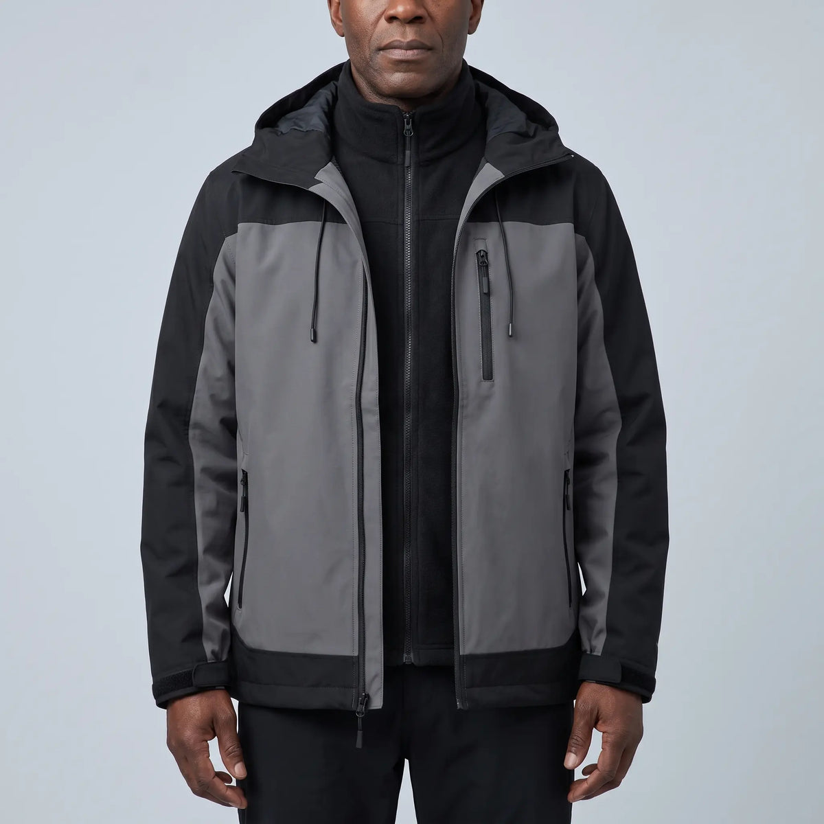 Men's grey waterproof hooded hiking jacket with black side panels, worn open over a black fleece