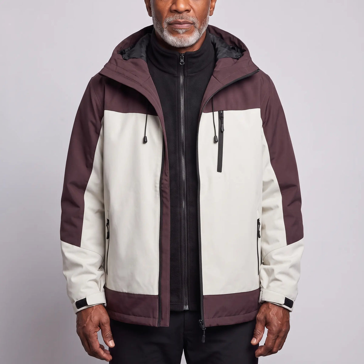 Men's white waterproof hooded hiking jacket with plum shoulder panels, worn open over a black fleece