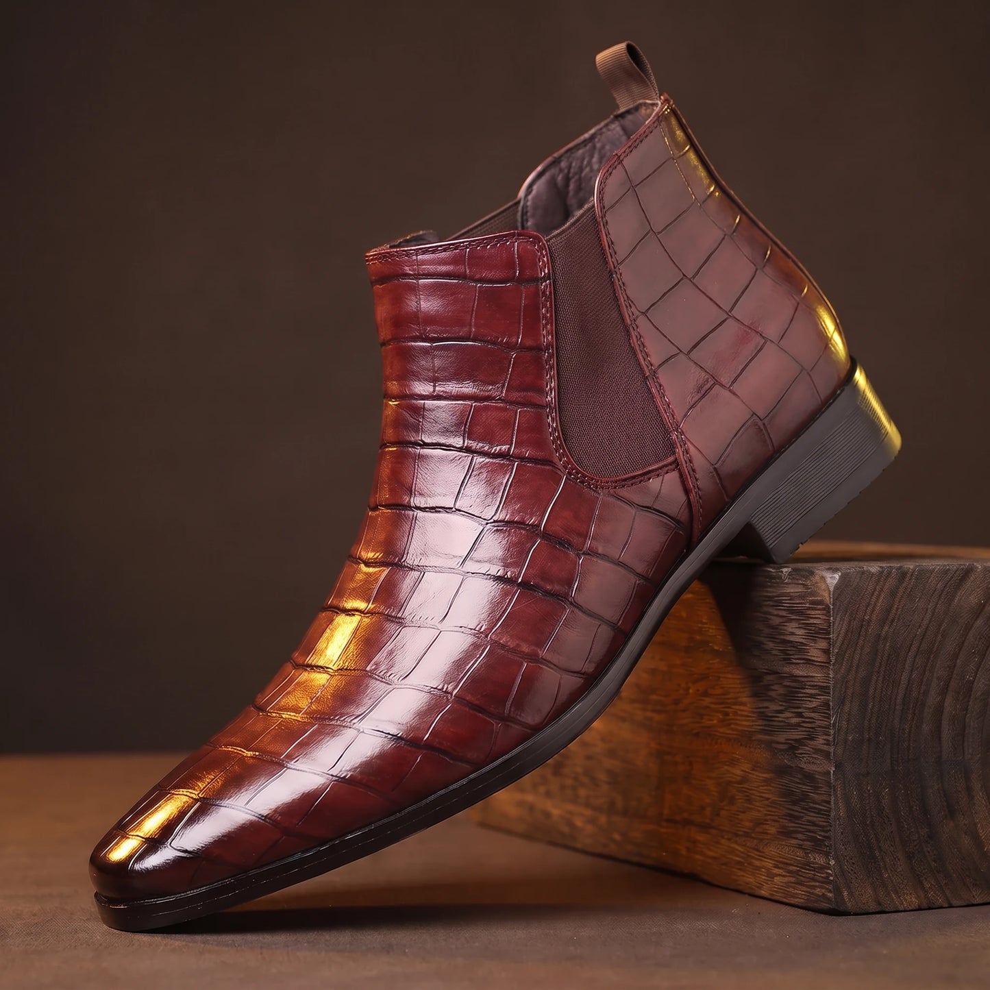 CROC GRAIN BOOTS wine-red croc-texture platform Chelsea boot on a smoked-oak block, moody amber light