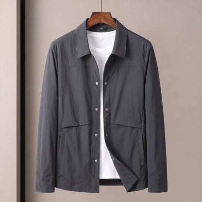 Crease Free Jacket in dark grey, a lightweight woven shirt jacket with a pointed collar, metal snap placket and welt hip pockets on a wooden hanger