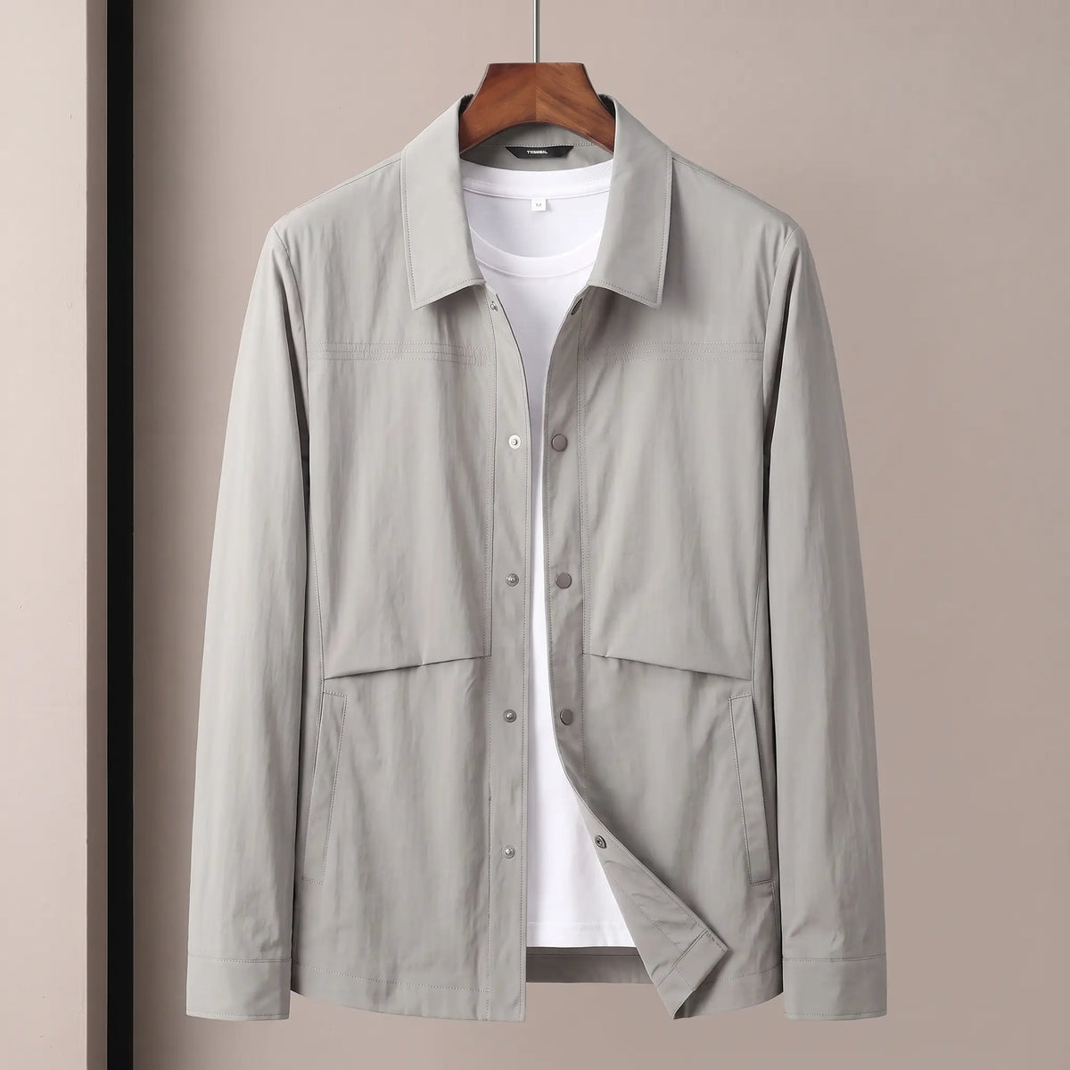 Crease Free Jacket in light grey, a lightweight woven shirt jacket with a pointed collar, metal snap placket and welt hip pockets on a wooden hanger