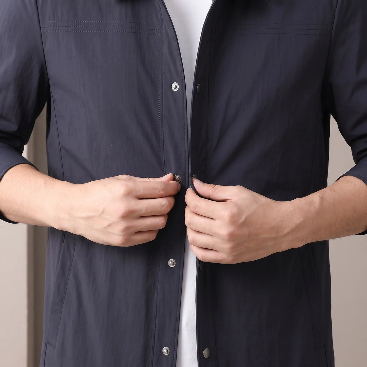 Man closing a metal snap on the navy Crease Free Jacket worn over a white tee