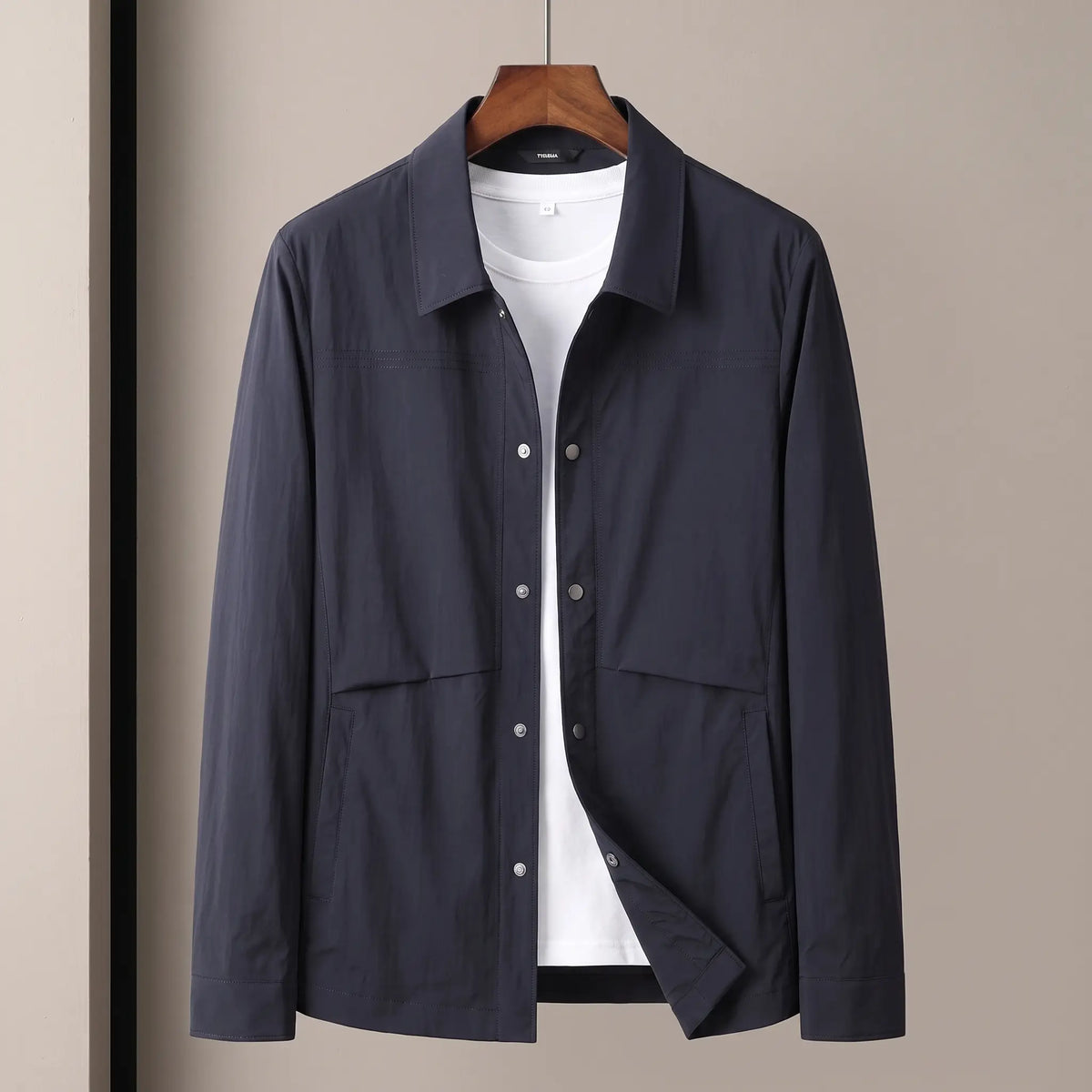 Crease Free Jacket in navy, a lightweight woven shirt jacket with a pointed collar, metal snap placket and welt hip pockets on a wooden hanger