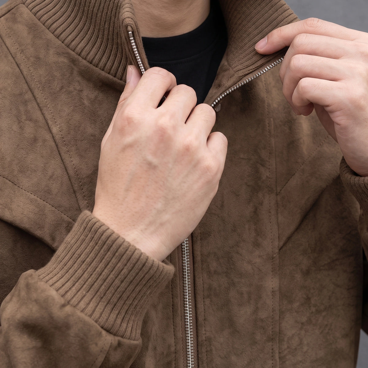 Man turning up the ribbed collar on the brown suede bomber jacket, close chest view