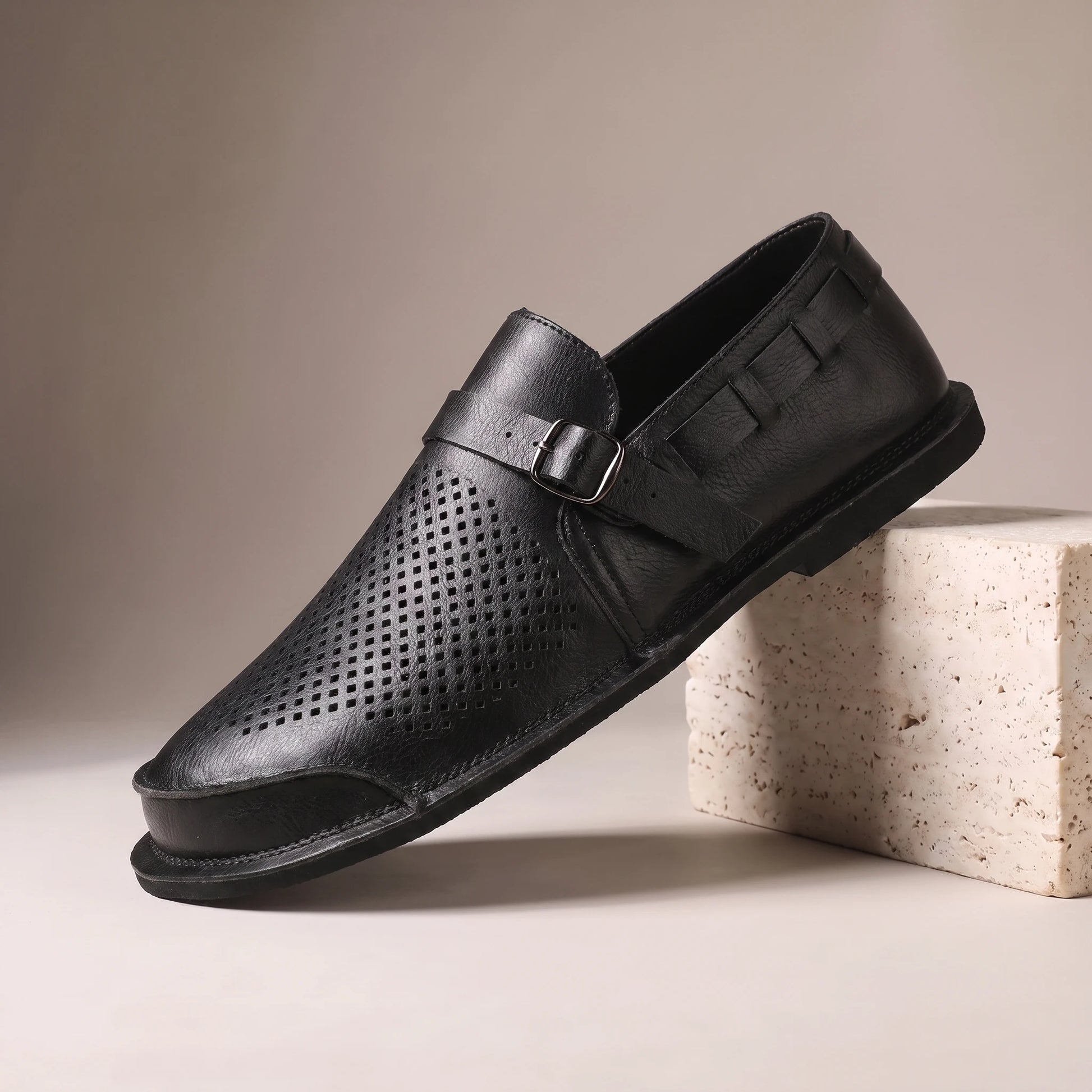 CLASSIC SLIP-ON LOAFERS black leather slip-on loafer with woven cut-out side panel on a travertine studio block
