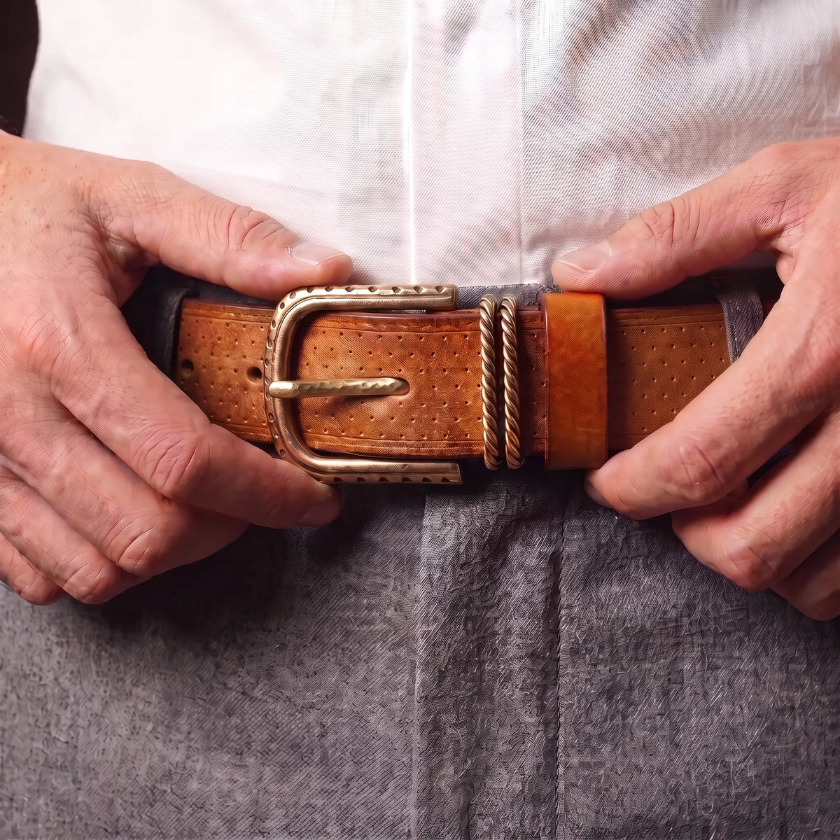 Man fastening the tan brass ring belt at the waist over grey trousers