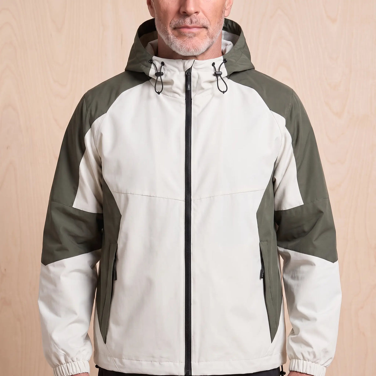 Beige hooded panel windbreaker with olive green colour block panels worn by a man, front view