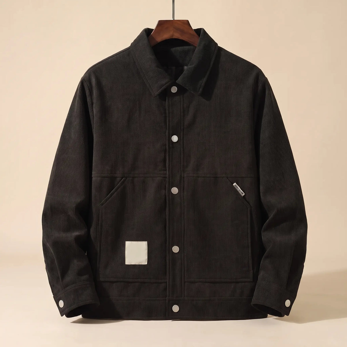 Black padded corduroy winter jacket with snap front on a wooden hanger, front view