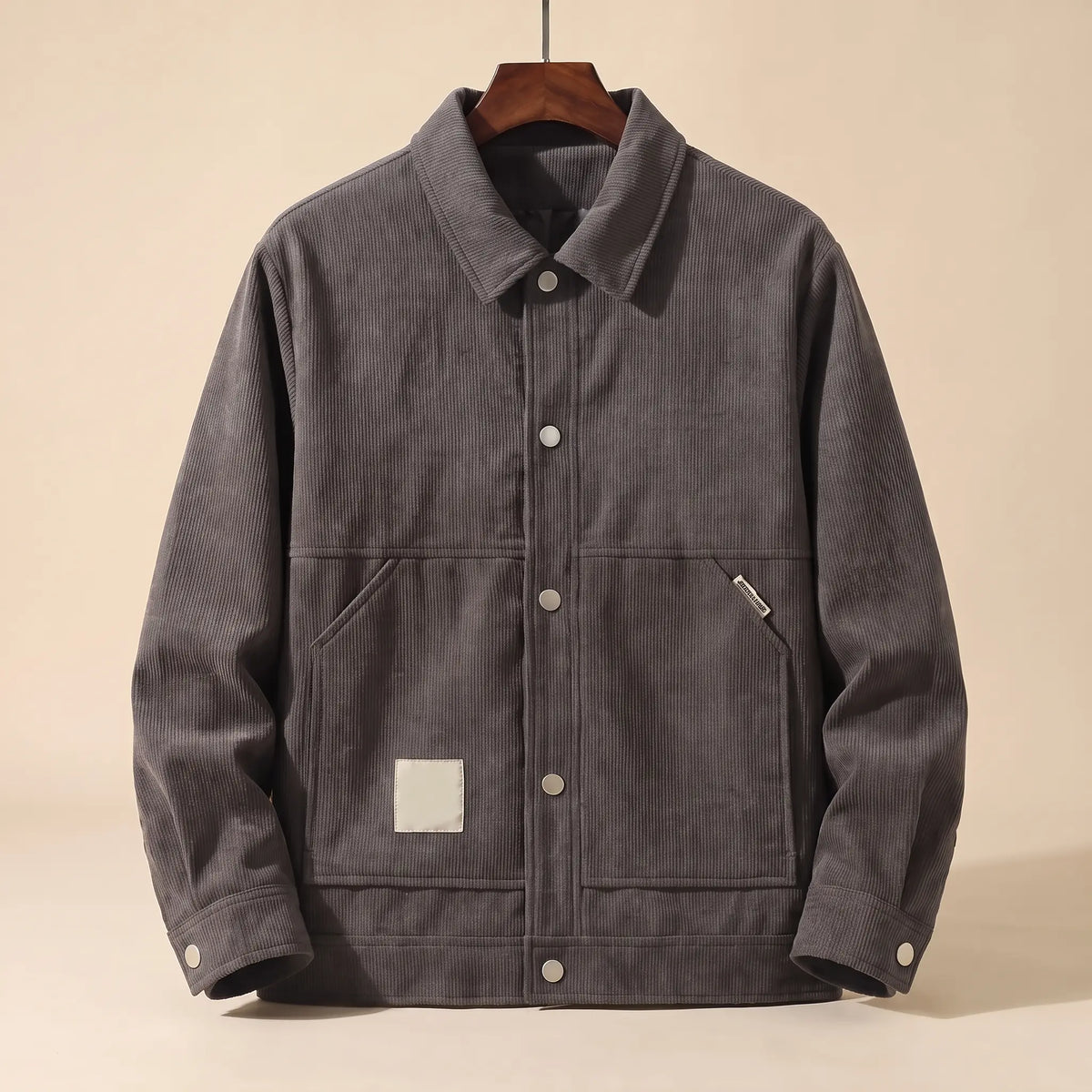 Grey padded corduroy winter jacket with snap front on a wooden hanger, front view