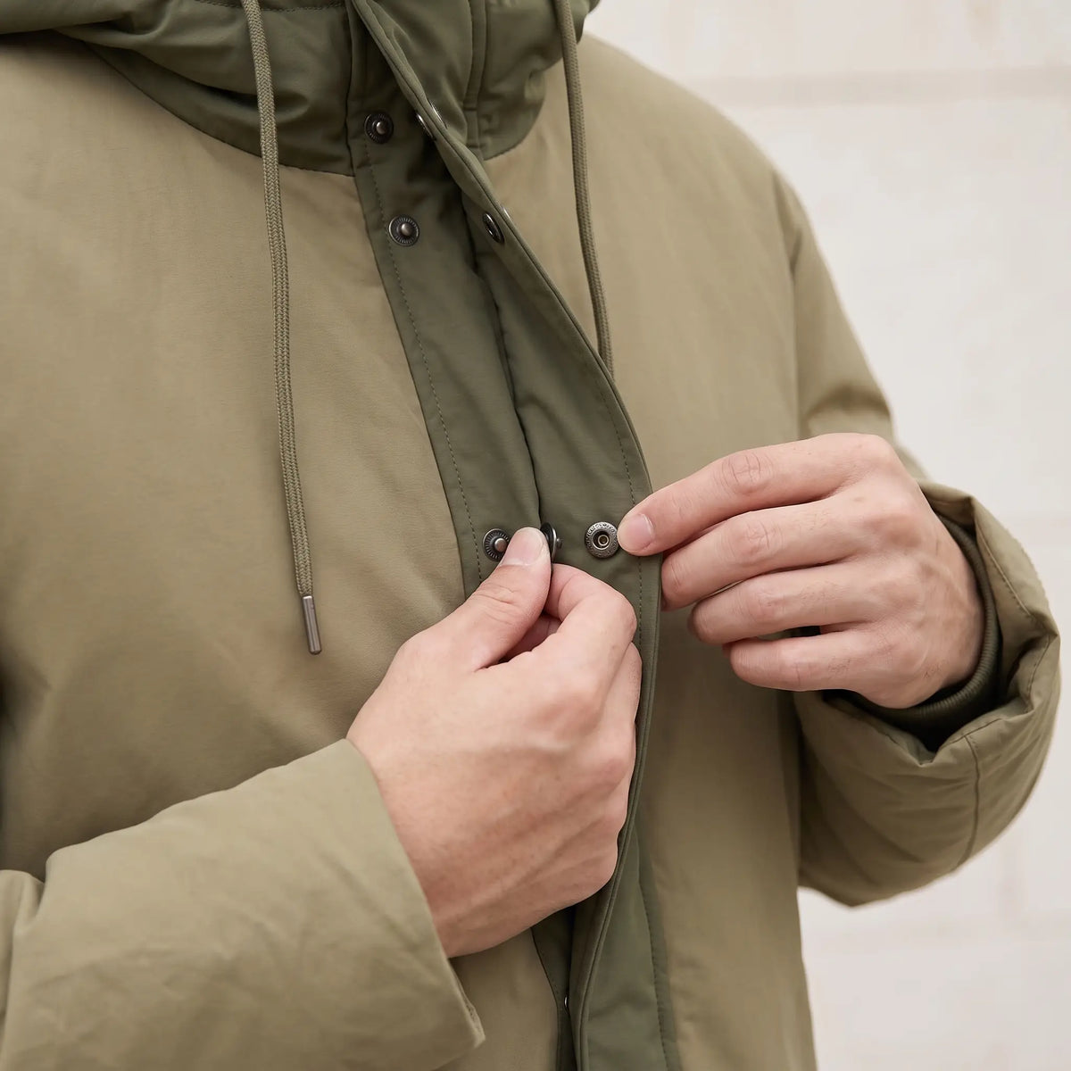Man closing a snap on the front of the khaki parka, close chest view
