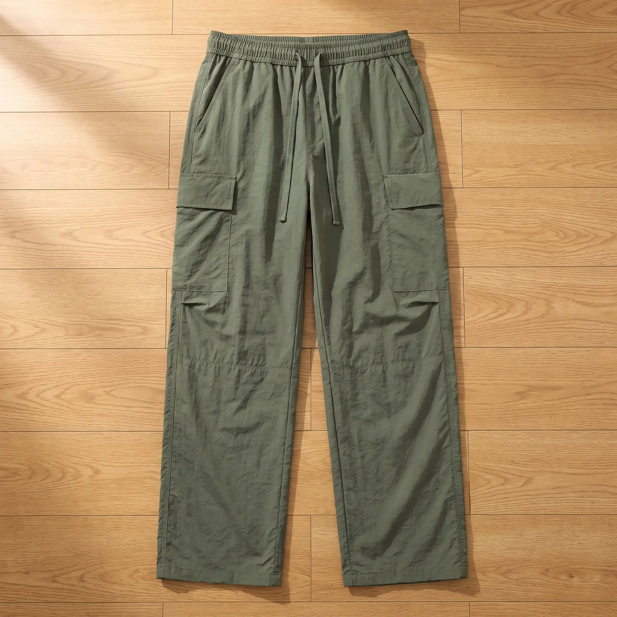Army green wide leg crinkle nylon cargo trousers laid flat on a wooden floor, front view
