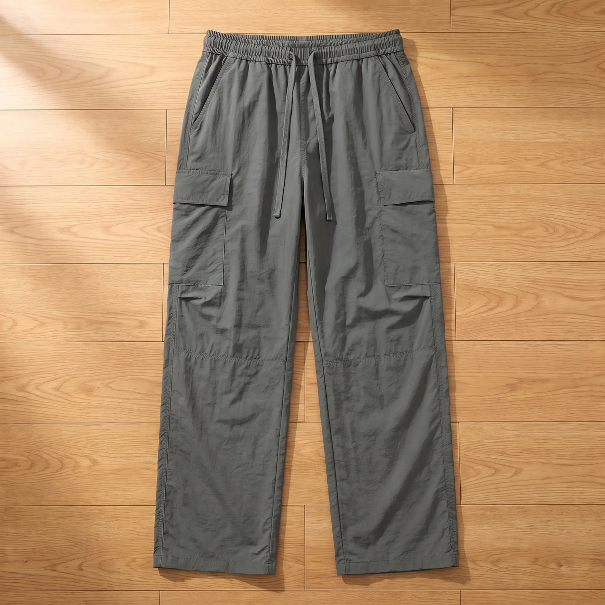 Grey wide leg crinkle nylon cargo trousers laid flat on a wooden floor, front view