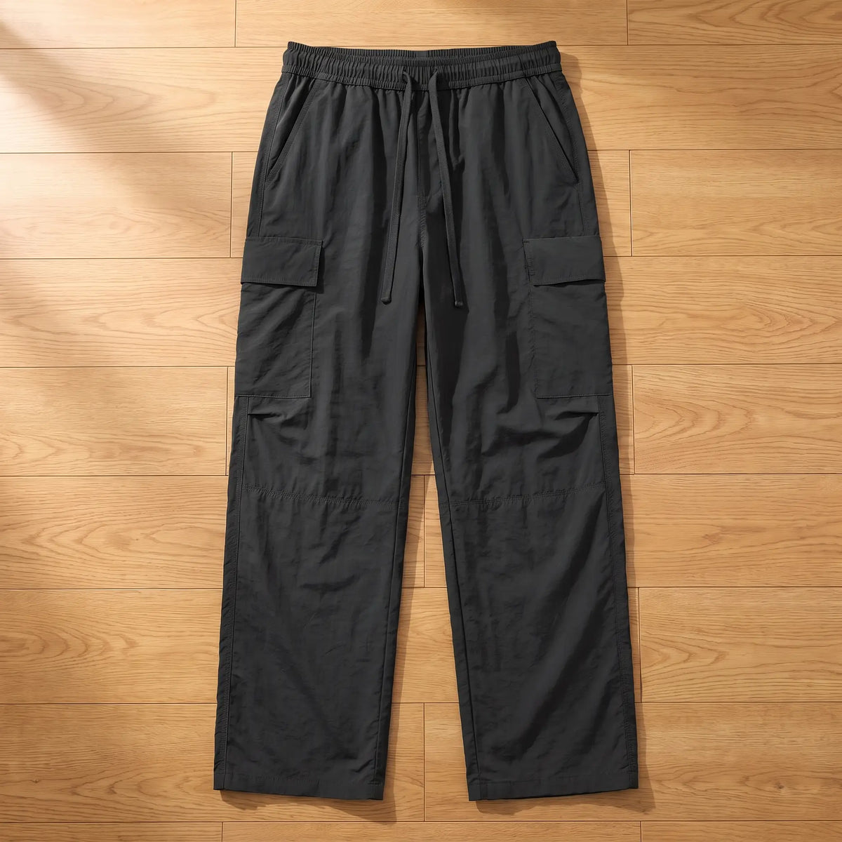 Black wide leg crinkle nylon cargo trousers laid flat on a wooden floor, front view