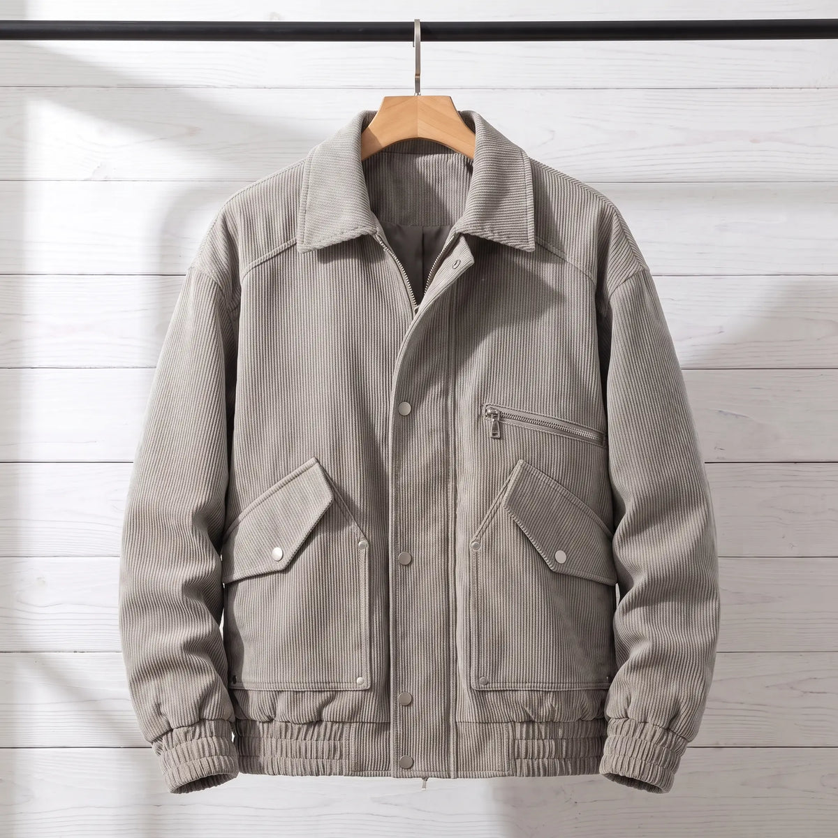 Light grey corduroy bomber jacket with snap front placket on a wooden hanger, front view