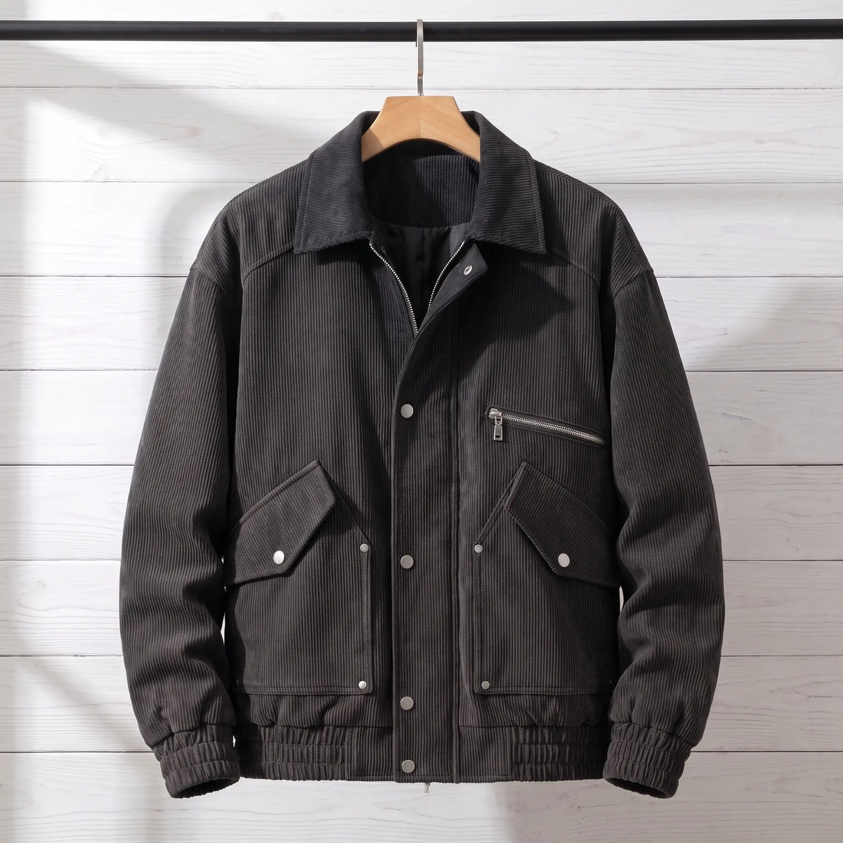 Black corduroy bomber jacket with snap front placket on a wooden hanger, front view